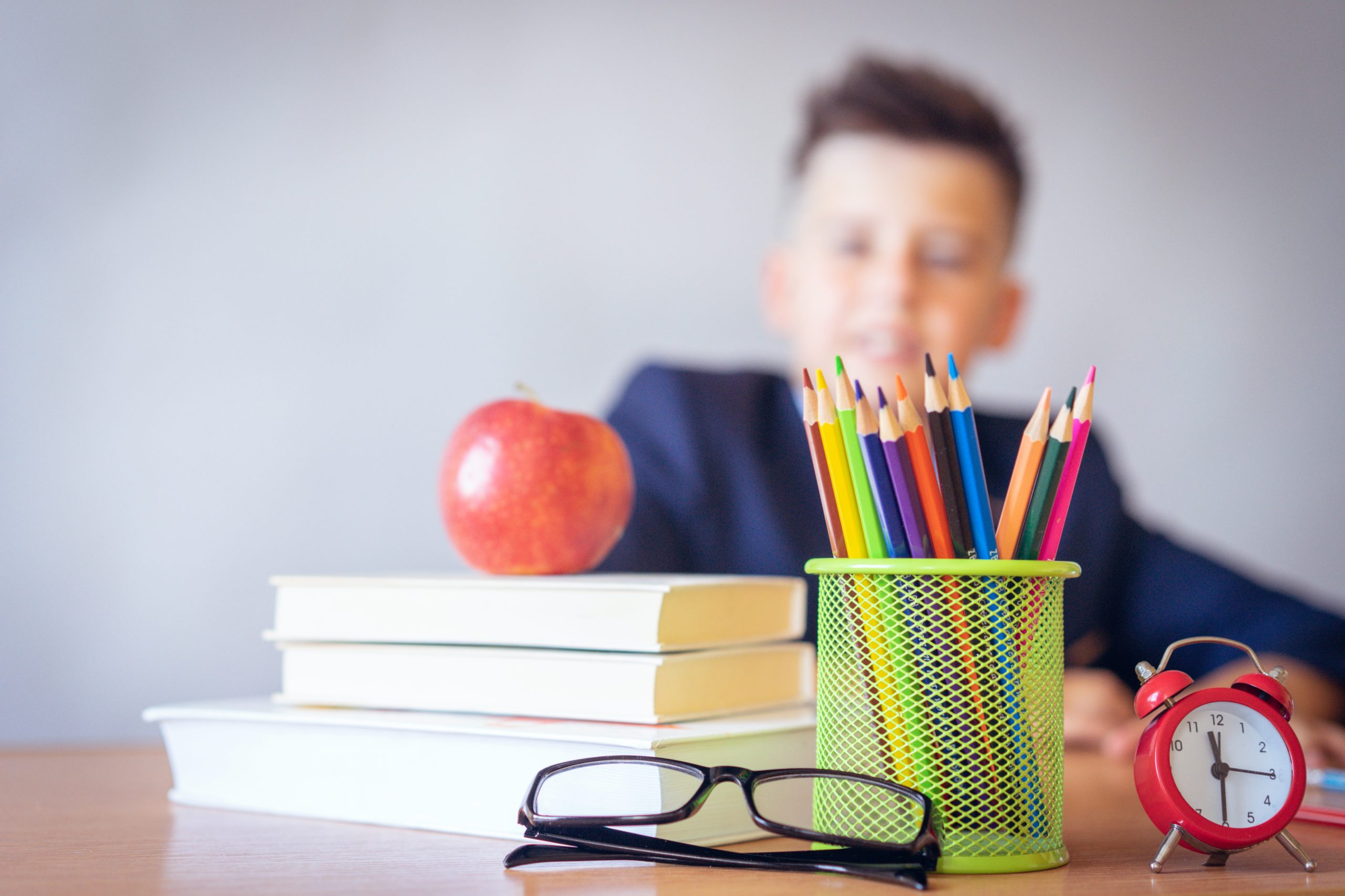 School supplies on a desk with a boy behind it